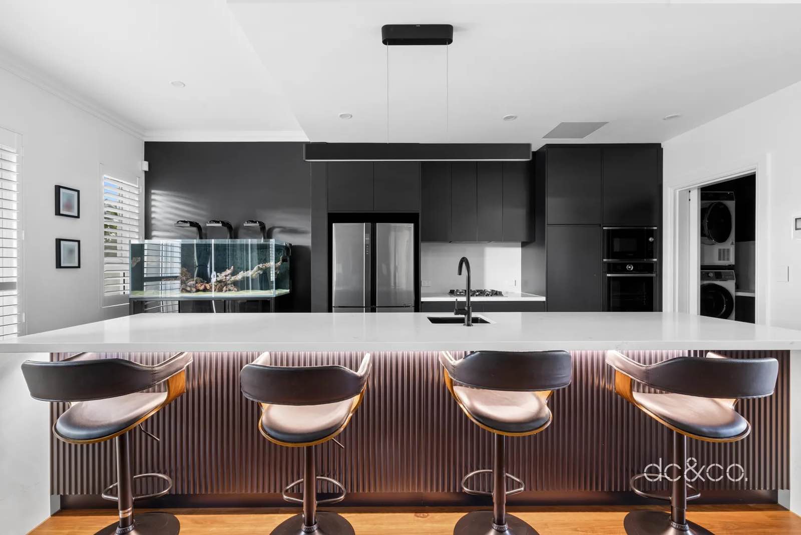 Kitchen island straight on, black cabinetry and stone benchtop with four stools