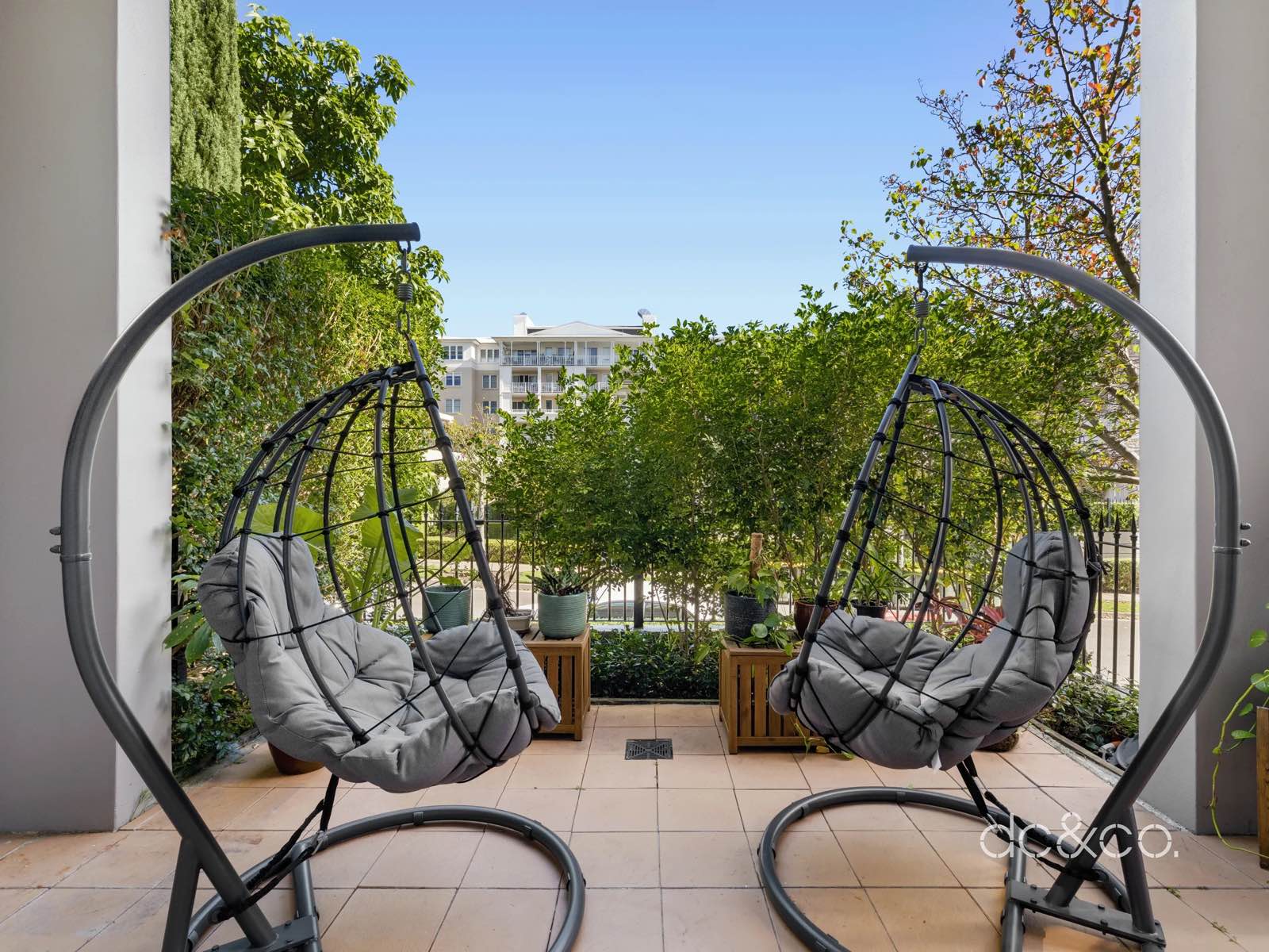 Two hanging chairs on the covered patio looking out through the hedge to the street