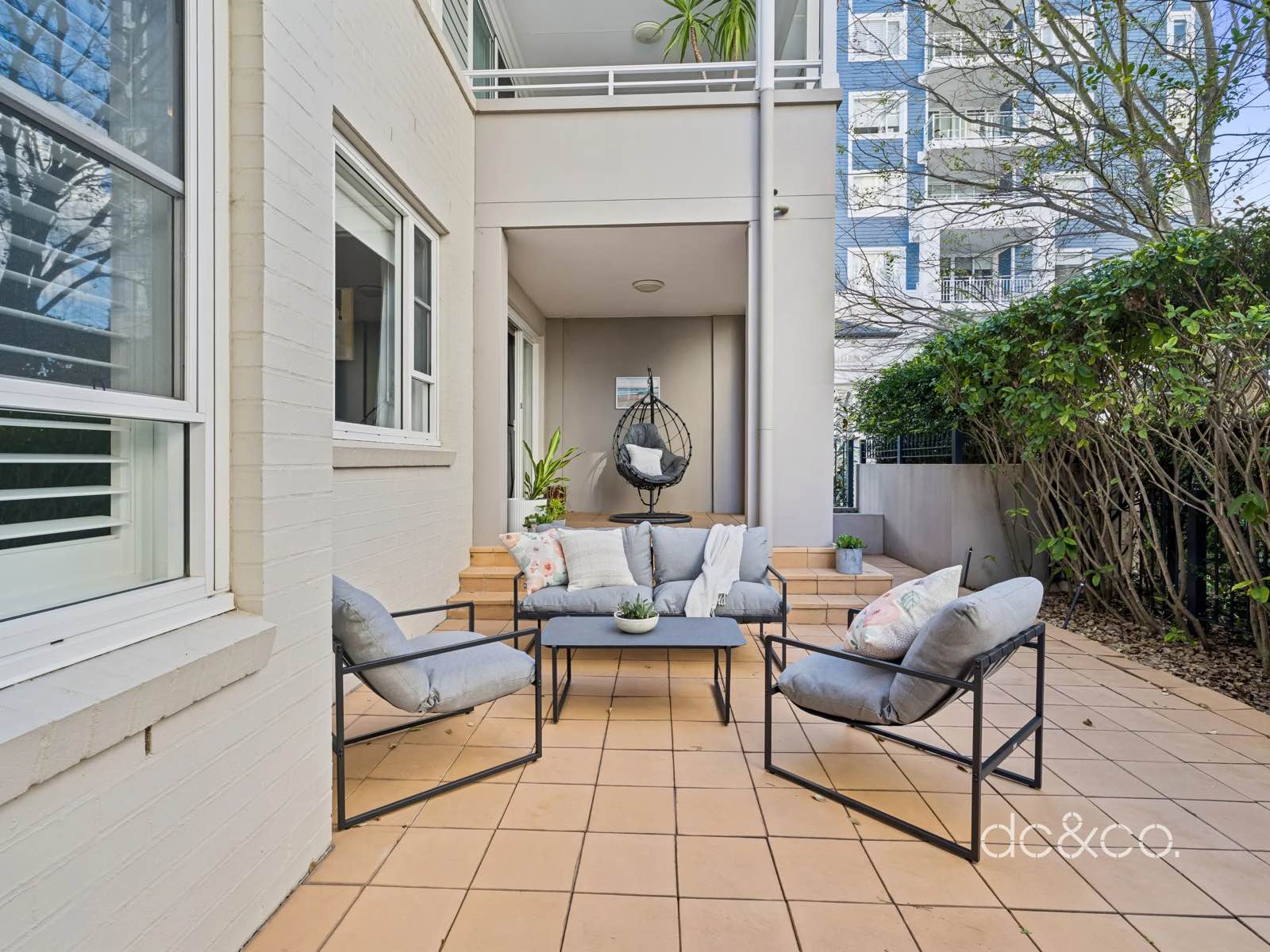 Covered patio with lounge seating, terracotta tiles and hedging on every side